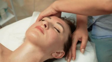 Kaplıcada kadın yüz masajı yaptırıyor. Masaj terapisti kozmetoloji salonunda cildini tazelemek için nazik yüz masajı yapıyor. Gevşemeyi ve kan dolaşımını arttırmak için hassas baskı uyguluyor.