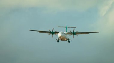 Pervaneli ve iniş takımlarıyla uçan turbo pervaneli uçak bulutlu bir havada uzanıyor. Mavi arka planda dönen pervaneli bölgesel uçak piste yaklaşıyor. Yolcu turbo pervanesi bulutların arasından iniyor.