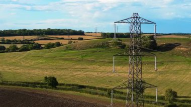Kırsal yamaçta elektrik iletim direği duruyor. Elektrik endüstriyel enerji altyapısından geçiyor. Çelik çerçeve kulesi kırsal arazide üstten güç iletkenleri taşıyor.