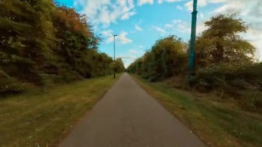 Mavi gökyüzü manzarasının altında yeşil çalılarla çevrili asfalt yolda bisiklet sürüyorum. Kalın çitlerin arasındaki kaldırımlı yolda birinci şahıs görüşlü sokak ışıklarıyla bisiklet sürüyorlar. Bulutlu gökyüzünün altında yapraklarla çevrili uzun düz yolda pedal çeviren bisiklet.