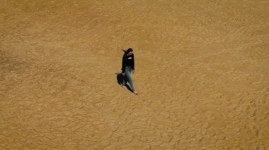 Çıplak ayakla boş kumlu sahilde gün ışığında gezinen bir kadın. Terkedilmiş bir plajda yüzeyi dokulu, yavaşça yürüyen bir kadın. Açık gökyüzünün altında altın kıyı şeridinde tek başına gezinen bir kadın.