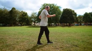 Adam İngiltere 'deki şehir parkında kulaklıklarda mutlu bir şekilde dans ediyor. Yetişkin bir adam, İngiltere 'de şehir yeşilliğinde neşeli bir şekilde müzik dinliyor. Orta yaş insanı, İngiltere 'nin eğlence alanında enerjik bir şekilde oyalanıyor. Halk parkında kulaklıkla mutlu bir şekilde dans eden adam