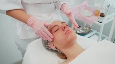 Cilt bakımı sırasında sakince uzanan bir kadın kozmetikçi masaj yaparken nazik hareketlerle yüz yüze gelir. Kadın, rahatlamak ve cilt esnekliğini geliştirmek için tasarlanmış profesyonel bakımdan keyif alıyor. Cilt rengini geliştirme amaçlı yatıştırıcı tedavi gören kız