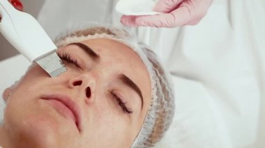 Güzellik uzmanı, estetik merkezde cilt bakımı sırasında ultrason cihazı kullanıyor. Kibarca arındırma ve canlandırma için gelişmiş bir araç uyguluyor. Müşteri, cilt dokusu ve su kaybının iyileştirilmesi üzerine odaklanarak profesyonel bakım görüyor