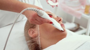 Güzellik uzmanı dermatoloji ofisinde cilt bakımı için ultrasonik kabuk soyma cihazı kullanıyor. Derinin berraklığını ve pürüzsüzlüğünü arttırmak için zararsız deri yüzme konusunda uzman. Gelişmiş yüz prosedürü uygulayan hasta yenilenmeye odaklanıyor.