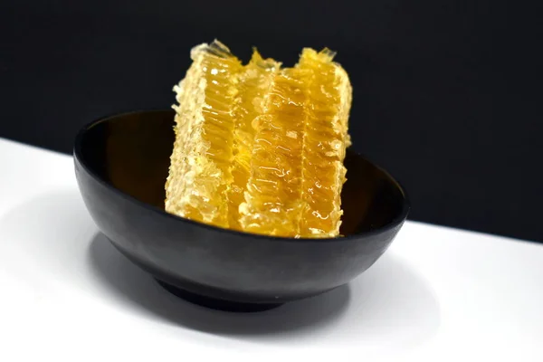 白色和黑色背景的黑色盘子里的梳子里的黄色蜂蜜 — 图库照片