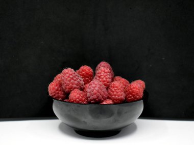 Siyah ve beyaz arka planda siyah bardakta kırmızı ahududular.