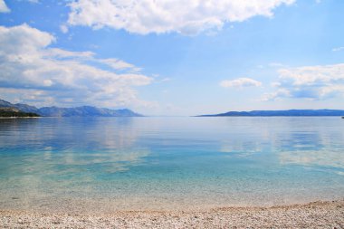 Güzel mavi gökyüzü, kumsaldaki sakin denizin üzerinde beyaz bulutlar.