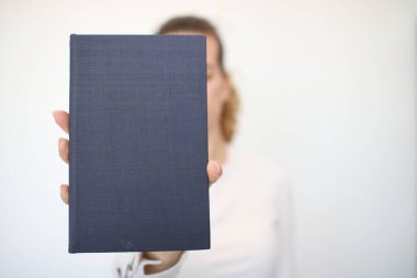 Genç bir kız elinde bir kitap tutuyor.