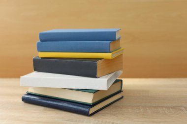 Tahta masanın üzerinde beyaz duvara karşı yığınla kitap.