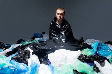 Çekici, saç kesimli, plastik torba çöpleriyle kaplı, koyu renk ışıklı arka planı olan genç bir adam..