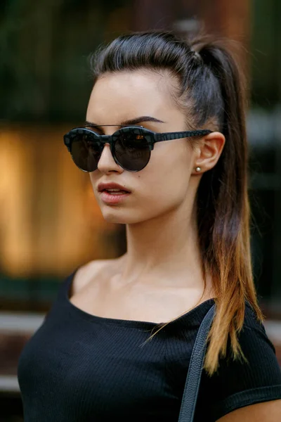 멋진 선글라스를 끼고 거리를 활보하는 소녀. 머리가 곱슬곱슬 한 아름다운 여자가 포니테일을 펴고 있다. — 스톡 사진