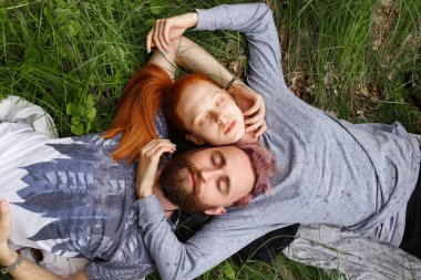 Bir çift portresi, yeşil bir çimen üzerine oturan, kapalı gözleri ile çevrilmiş. Çift ilişkisi.