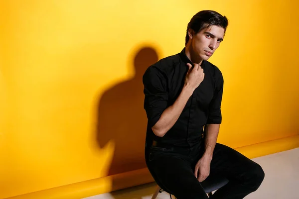 黄色の背景に椅子に座って黒い服を着たハンサムな若い男のクローズアップ肖像画 水平方向 — ストック写真
