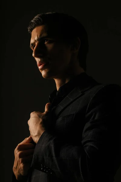 Vertical view. Business man dressed in black suit portrait against a dark background.