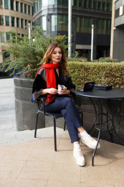 Elinde tatlı tutan günlük kıyafetli, kızıl saçlı bir kadın açık bir kafede otururken yemeye ve tatmaya başladı. Dikey görünüm.