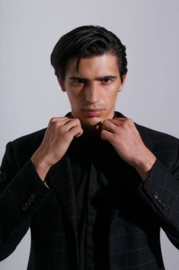 Beyaz arka planda siyah giysili, kendinden emin genç bir adam. Dikey görünüm.