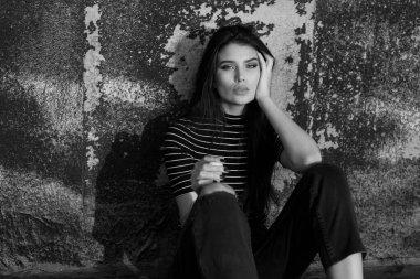 Moda görünümlü, düz saçlı, kameraya bakan, çatıda oturan ve sigara içen genç bir kızın siyah beyaz görüntüsü..