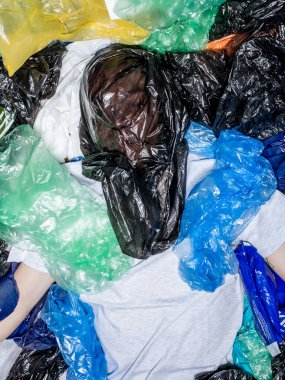 Yüzünde naylon torbayla uzanmış, etrafı plastik poşetlerle çevrili genç bir adamın üst görüntüsü. Yatay görünüm.