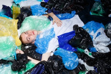 Mavi gözlü, uzanmış, burnunda halkayla, plastik poşetlerle kameraya bakan genç bir adamın üst görüntüsü..