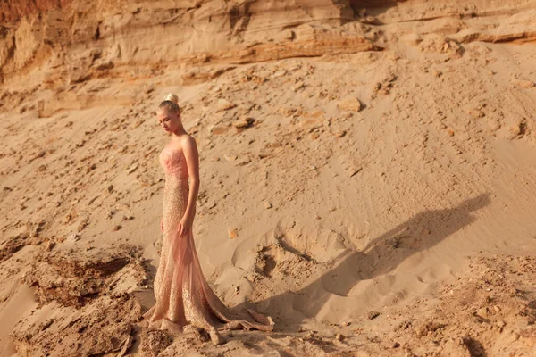 Female model in splendid gold dress posing in desert, over sand career background. Space for text.