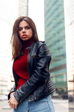 Makyajlı, deri ceketli, şehirde dolaşan güzel esmer kızın yakın plan portresi. Yaşam tarzı konsepti. Dikey görünüm.