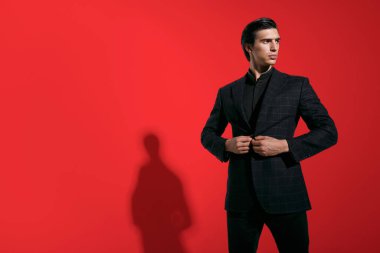 Yatay görüş. Kırmızı arka planda siyah şık takım elbiseli yakışıklı esmer adam. Boşluğu kopyala.