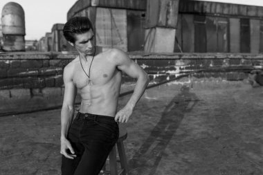 Siyah beyaz fotoğraf. Gün batımında binaların arka planında güçlü ve atletik vücudu olan yakışıklı bir gencin portresi..