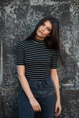 Düz kahverengi saçlı, modern kıyafetler giymiş, makyajlı, siyah bir duvarla desteklenen neşeli bir kızın güzel ön portresi..