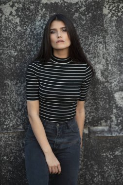 Düz saçlı, modern kıyafetler giymiş, makyajlı, duvarla desteklenen neşeli bir kızın güzel ön portresi. Dikey görünüm.