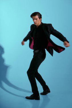 Siyah takım elbiseli, mavi arka planda tek başına dönen yakışıklı bir genç portresi..