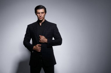 Gri arka planda izole edilmiş siyah takım elbiseli yakışıklı genç adamın ön portresi. Yatay görünüm.