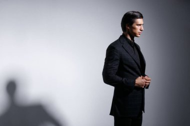 Siyah takım elbiseli yakışıklı genç adamın portresi, koyu gri arka planda..