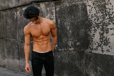 Yaşlı siyah duvarın yanında üstsüz, yakışıklı genç bir adam, aşağı bakıyor. Sportif sağlıklı bir adam..