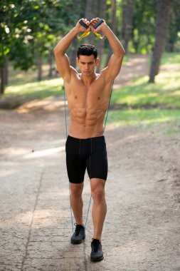 Spor giyimli yakışıklı bir adamın parkta spor yaparken ön görüntüsü. Sağlıklı yaşam tarzı kavramı. Dikey görünüm.