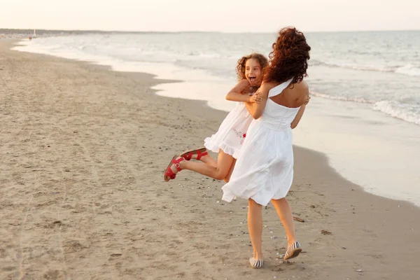 Yatay görüş. Anne, kızını sahilde kucaklıyor. Tatilde ve seyahatte mutlu bir aile. Anne sahilde kızını kucaklıyor ve oynuyor..