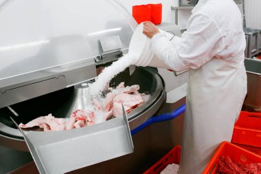 Endüstriyel et işleme fabrikasında çalışan bir işçinin kırpılmış görüntüsü, ham ürün hazırlama sürecine baharatlar ekliyor.