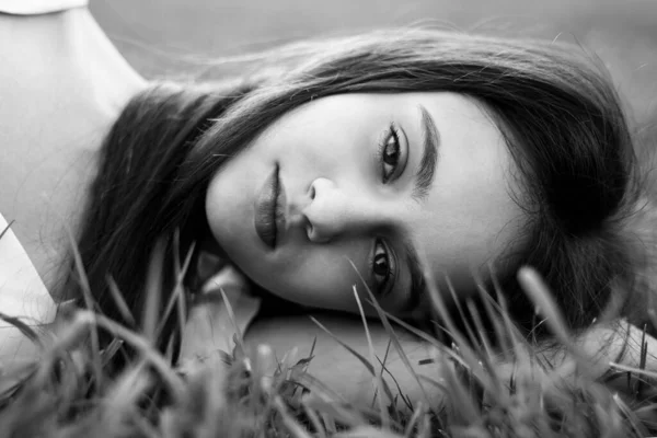 Beautiful young girl lying on grass, looking at camera. Black and white image. — Stock Photo, Image