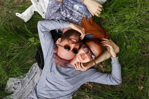 Retrato de um belo casal, sentado em uma grama verde, sentado em óculos de sol . — Fotografia de Stock