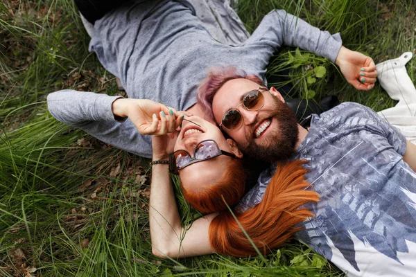 Sorrindo casal hipster, sentado em uma grama verde, sentado com as cabeças viradas com os olhos fechados . — Fotografia de Stock