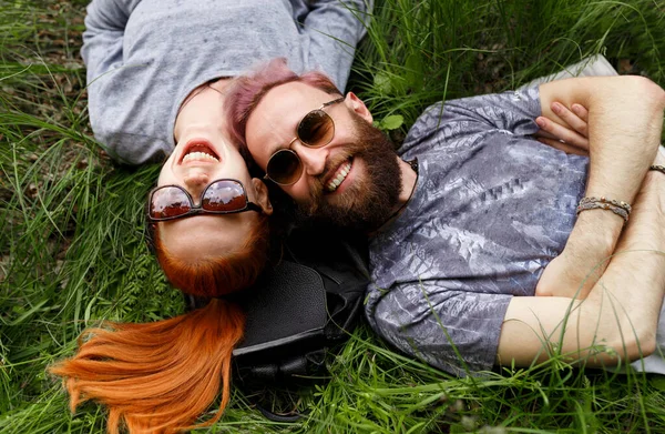Vista superior de um par, sentado em uma grama verde, sentado com a cabeça virada desgaste em óculos de sol . — Fotografia de Stock