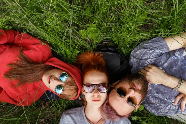 Visão superior de um sorriso desfrutando de jovens em óculos de sol, deitados em uma grama, usam óculos de sol, olhando para a câmera . — Fotografia de Stock