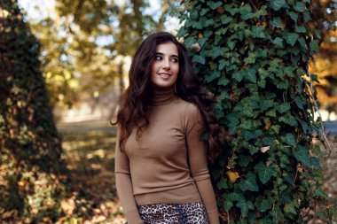 Güzel profil portresi. Güzel esmer bir kadın güz giysileri içinde, makyajlı, gündüz vakti parkta poz veriyor..