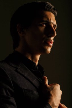 Dikey görünüm. Siyah takım elbiseli yakışıklı adam koyu bir arka planda..