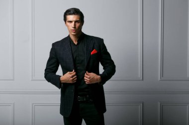 Beyaz arka planda, cebinde kırmızı ipek eşarp olan siyah takım elbiseli, kendinden emin bir gencin ön portresi..