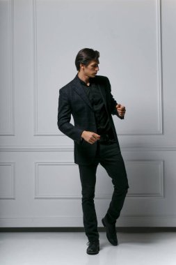 Dikey görünüm. Zarif genç moda adamı beyaz arka planda kameradan uzak bir şekilde takım elbisesini ayarlıyor..