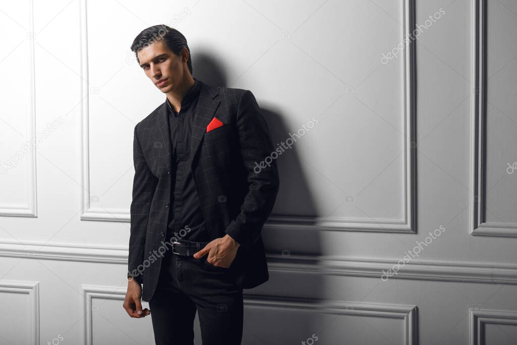 Confident handsome young man in black suit with red silk scarf in pocket, over white background.