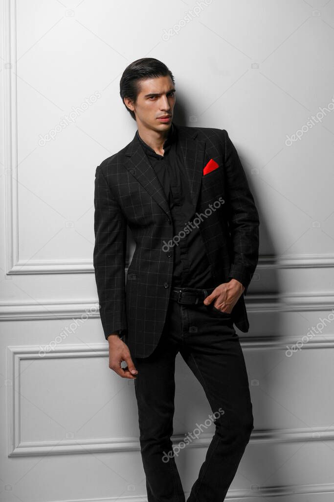 Vertical portrait of confident young man in black suit with red silk scarf in pocket, over white background.
