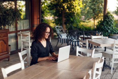 Terasta dizüstü bilgisayarda yazan masada oturan güzel genç kadının profil portresi..