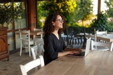 Terasta dizüstü bilgisayarda yazan gülümseyen genç kadının profil portresi..